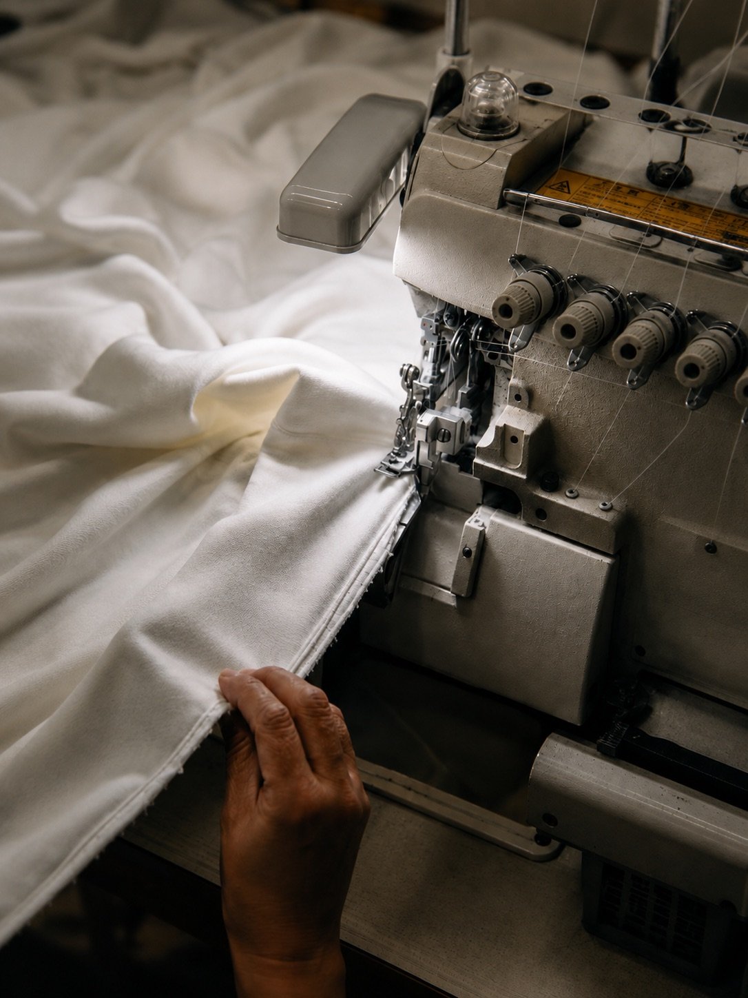 A machinist guiding cream fabric through an overlock machine on the production floor at Marah Fashion Group